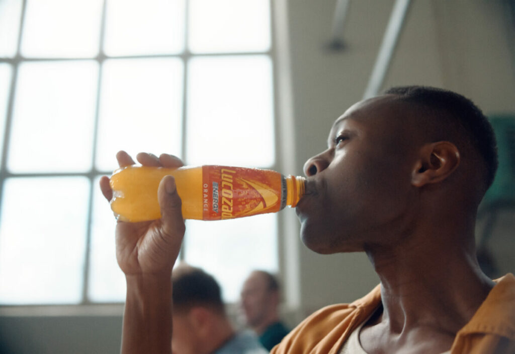 Lucozade has unveiled a new masterbrand platform which unites its three key drinks, and will be supported by a campaign across TV, social, in-store activation, consumer sampling and more. The image is from the accompanying TV campaign and shows a man in a sports hall drinking Lucozade Orange, with relish.
